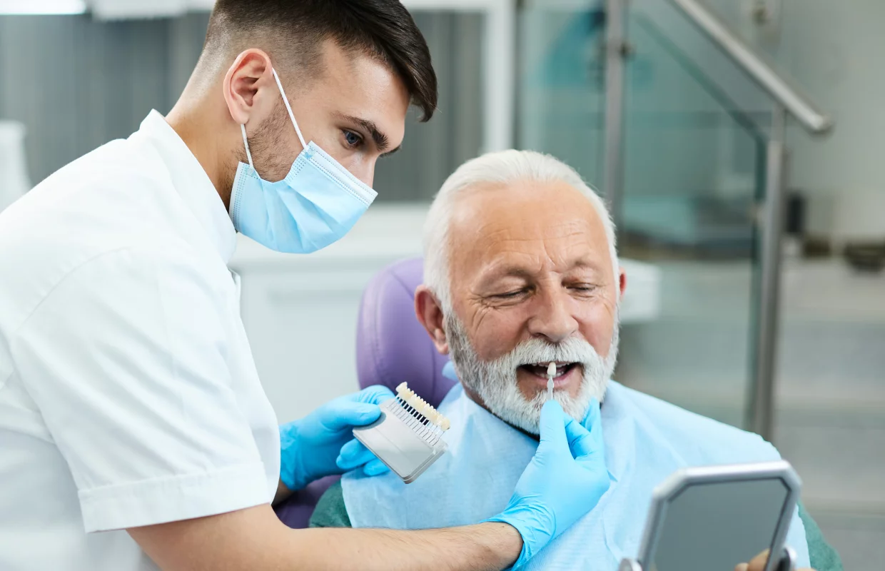 Der Zahnarzt passt die Zahnersatzfarbe gemeinsam mit seinem älteren Patienten an